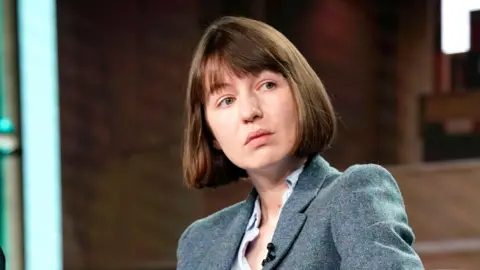 Sally Rooney says she will support Palestine Action despite ban Getty Images Sally Rooney, who has short brown hair and a fringe, and is wearing a woollen suit jacket and a shirt, listens to someone speak.
