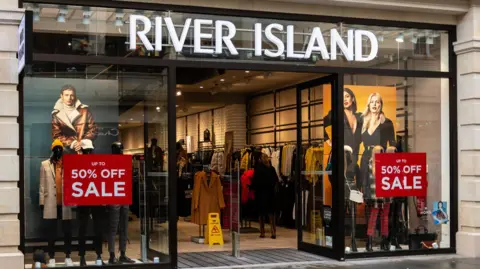 River Island allowed to shut shops to stave off collapse Getty Images A River Island shop front, with red "50% off sale" signs in the windows.