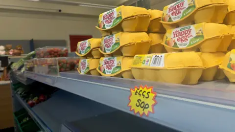 Southampton social supermarket alternative to food banks BBC A stack of eggs in yellow boxes on a supermarket shelf. The packaging reads "the happy egg company", and below is a hand-written sticker that reads "Eggs 50 pence."