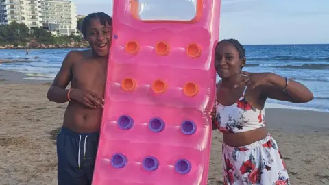 Family's tribute to Birmingham siblings who drowned in Spain Family Ameiya (R) and Ricardo Del Brocco (L) on holiday. They are either side of an pink inflatable. They are on a beach and smiling. Ameiya has short dark hair and wears a two piece costume of white with a floral design. Ricardo has short dark hair in braids and wears a blue pair of shorts.