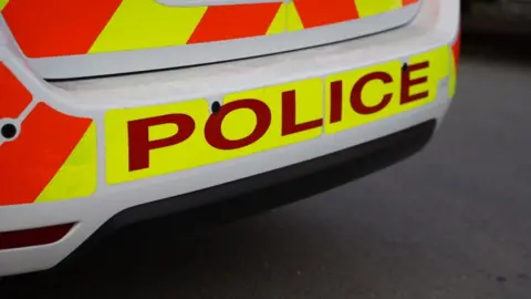 Teenager arrested after death of 13-year-old girl in Huddersfield BBC Stock image showing the rear bumper of a police car, with POLICE in large red letters against a yellow background.