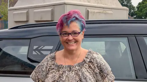 Somerset food banks say demand is rising as donations drop Alison Pope Alison Pope stands against a black car, she is wearing glasses and has a leopard print top. Her hair is dyed blue and pink.
