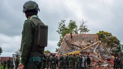 A fierce war of words keeps the two countries on edge Getty Images A Cambodian soldier stands on guard near a destroyed building at the border between Thailand and Cambodia. He watches a team of soldiers and officials inspecting the site.