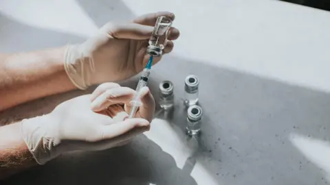 Government turns to TikTokers to advise on cosmetic surgery abroad Getty Images A gloved medical professionals' hand uses a syringe to extract liquid from some vials on a table.