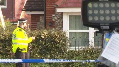High Wycombe man who shot PC with crossbow jailed A police officer is stood near a fenced-off front garden of a house. There is also blue and white police tape.