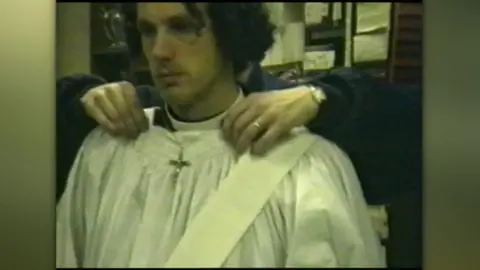Ex-priest Chris Brain found guilty of 17 indecent assaults The Nine O'Clock Trust A man has white vestments put on him by a figure from behind. A crucifix is worn round his neck.