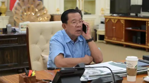 A fierce war of words keeps the two countries on edge Hun Sen/ Facebook Hun Sen in a half-sleeved blue shirt at his desk, talking on the phone.