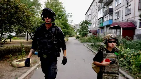 Inside Donetsk as residents flee attacks on Ukrainian region Putin wants to control BBC News Two people - a tall man in black and a small woman in khaki camouflage gear, both wearing padded body warmers and dark sunglasses - walk down a residential street. Neither are smiling