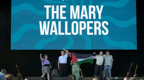 Bands boycott Victorious music festival after group 'cut-off' Getty Images Multiple members of The Mary Wallopers stood on the Victorious Festival stage holding a Palestinian flag and with mouths open and arms raised appearing to chant. Behind them is a large screen with their band name on.