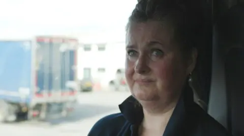 Lives torn apart by fatal crashes on the A9, Scotland's longest road Elaine MacKenzie has fair hair which is tied up and she is wearing a dark blue fleece. She is pictured inside the cab of her lorry and there is a lorry, slightly out of shot, visible outside her window parked in a lorry park.