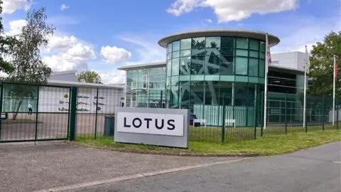 Sports car manufacturer Lotus to cut 550 jobs at Norfolk base Martin Giles/BBC The outside of the Lotus building in Hethel, near Wymondham. The building is a curved glass building with a sign outside the front which says LOTUS in black letters.