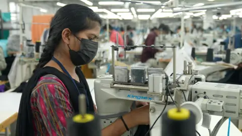 Inside the Indian factories hit hard by US's 50% tariffs Vishnu Vardhan, BBC News A young woman, wearing a multi-coloured dress with a mask, intently working on a sewing machine at a factory in southern India.