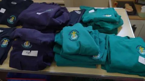 South East parents face struggle to afford school uniform Peter Whittlesea / BBC A table with school uniform on it. The uniforms are navy blue and turquoise and have a school badge on it.