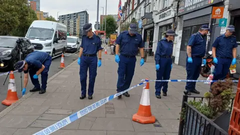 Boy and man arrested over Gants Hill restaurant 'arson attack' PA Media A row of six uniformed police officers search an area on Woodford Avenue in Ilford. They are in a line and looking down or to the side, working their way along a section of pavement cordoned off by police tape. Parked cars are in the road to the left and a row of businesses can be seen along the right hand side.