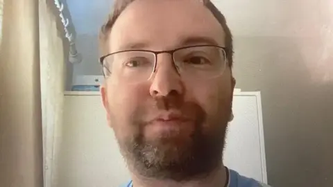 Coventry City Football Club purchases CBS Arena A man is wearing a blue top and glasses. He has brown hair and a beard.