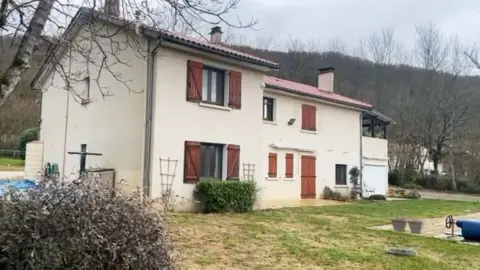 Actor son of 'murder-suicide' victim issues stepdad funeral plea A white house with windows with brown shutters and a green lawn, with trees and hills in the background