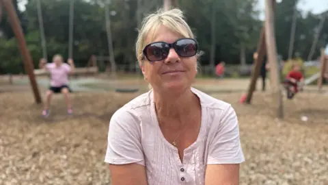 Summer holiday childcare costs a struggle, Guernsey parents say a woman in her late 50's wearing a light pink cotton top. She wears round sunglasses and has blonde hair up in a ponytail