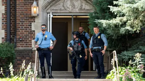 Minneapolis school shooting: What we know Reuters Four police officers, three with bulletproof vests and one with a helmet and gun standing outside an open entrance. There are steps leading to the doorway