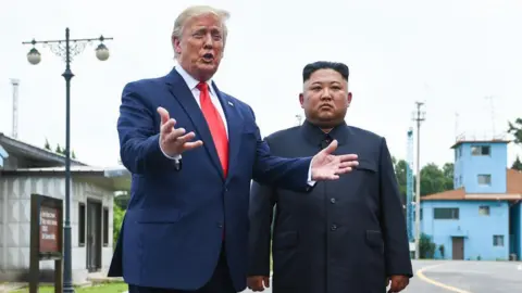 South Korea's Lee Jae Myung turns charm on during Trump meeting Getty Images Standing on a road in the Joint Security Area, Trump gestures with his hands as he speaks, wearing a navy suit and red tie. Beside him stands Kim Jong Un, wearing a black button-up suit, looking solemn with his hands by his side.