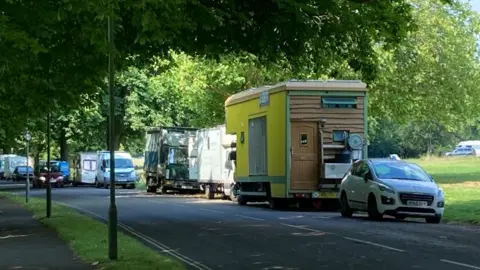Bristol council writes to deputy PM for van dweller help A row of campervans, trucks and cars line a street on the Bristol Downs with a green field in the background.