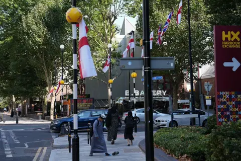 The questions about St George's and union jack flags lining British streets AFP via Getty Images St George's flags and Union Jack flags hang from lampposts and a zebra crossing light on a street in London.