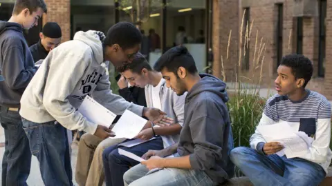GCSE grades 2025: The 9-1 boundaries explained Getty Images A group of male students sit outside a school or college building opening their exam results.