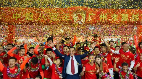Chinese property giant to be delisted after spectacular fall AFP via Getty Images Gold and pink confetti rains down as head coach Fabio Cannavaro of Guangzhou Evergrande and his players celebrate winning the 2019 Chinese Super League title on 1 December, 2019 in Guangzhou, Guangdong Province of China.