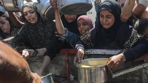 Humanitarian groups call on Israel to end 'weaponisation of aid' in Gaza EPA Internally displaced Palestinians, including children, hold pots as they receive food from a charity kitchen