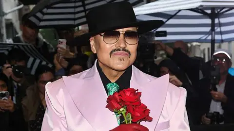 Willy Chavarria sorry after Adidas shoe cultural appropriation row Getty Images Willy Chavarria on a red carpet with photographers all around wearing a black hat, sunglasses and a pale pink tuxedo with exaggeratedly large lapels and holding three red roses