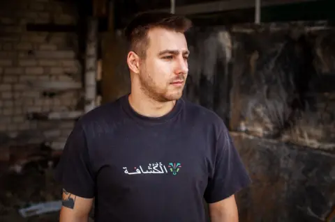 They escaped Ukraine's frontlines. The sound of drones followed them Stanislav Ostrous/BBC Dmytro Olifirenko wears a dark T-shirt with a scrawled logo in white and a tattoo partially showing on one arm