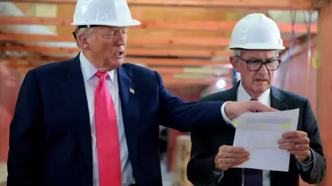 Why this row could rattle the US economy Chip Somodevilla/ Getty Images US President Donald Trump and Federal Reserve Chair Jerome Powell tour the Federal Reserve’s headquarters renovation project on July 24, 2025. Both men are wearing white hard hats, and suits, as Trump points at a piece of paper Powell is holding, which both men are looking at.