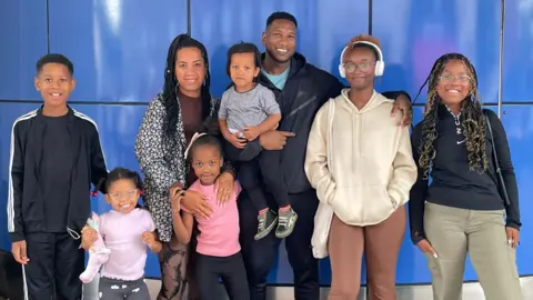 Do cash rewards or gifts boost exam grades? Leon Smith The Smith family of eight stand looking at the camera. They all have their hands around each other and are smiling.