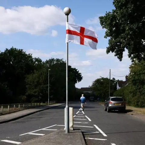 The questions about St George's and union jack flags lining British streets Reuters A flag of St George hangs from a lamppost on an island in the middle of an empty road, as a man walks down the road in the background.