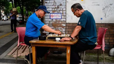 Getty Images Two men play Janggi, sometimes called Korean chess, on a street in Seoul on July 1, 2025. 