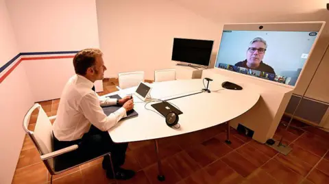 Kremlin plays down Zelensky talks as Trump warns Putin may not want 'to make deal' Getty Images Emmanuel Macron sits at a table in front of a video conferencing screen. Macron has short brown hair and wears a white shirt and dark suit trousers. He is sat at a round white table in a white-walled room with brown tiled flooring. At the other end of the table is a large screen on which a video conference is being held. Sir Keir Starmer is enlarged on the screen, while a row of small boxes containing the other participants sits below him. Starmer wears a grey top and black-rimmed glasses, and sits in front of a plain white background.
