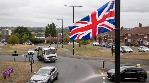 The questions about St George's and union jack flags lining British streets Getty Images A Union Jack flag hangs from a lamppost above a roundabout, as cars pass beneath it and houses and other flags hanging from lampposts can be seen in the distance.