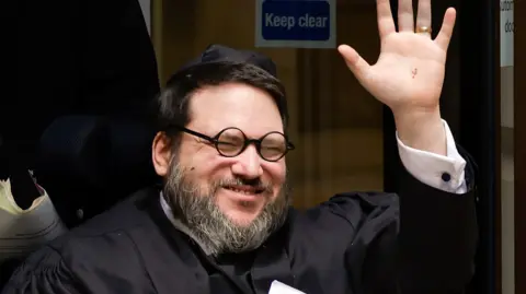 Fugitive Nicholas Rossi guilty of rape after extradition to US Getty Images Head and shoulders of a smiling Nicholas Rossi, who is being pushed in a wheelchair. He waves and is wearing a wedding ring. He wears black circular glasses, a white shirt and what appears to be a black judges' gown.