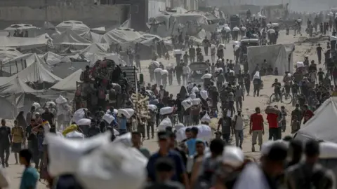 Eleven more die from malnutrition in Gaza, Hamas-run health ministry says EPA A landscape image of a dirt track with a number of people walking and carrying white aid packages. Tents can also be seen.