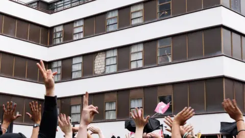 Behind the wave of asylum hotel protests Dan Kitwood/Getty Images Anti Fascist protesters cheers and wave as men believed to be migrants gesture from a window of the Barbican Thistle Hotel as anti-immigration, 'stand up to racism' and 'anti-fascist' groups all gather outside on August 2, 2025 in London, England.