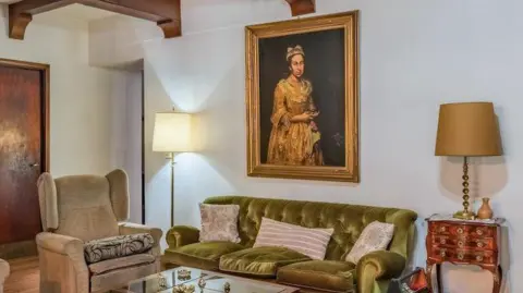 Artwork looted by Nazis 80 years ago spotted in estate agent ad Robles Casas & Campos An interior shot showing a living room with a green sofa against a white wall, flanked by two lamps. A portrait hangs on the wall behind the sofa.