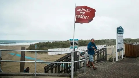 Hurricane Erin's high waves thrash coast of North Carolina Reuters A man in a sweat-suit and flip flops walks away from stairs leading to a beach in Avon-by-the-Sea, New Jersey. Next to him his a red flag reading 'Danger Rip Currents'. The sky ion the background is overcast as Hurricane Erin nears the east coast.