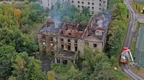 Girl, 14, arrested over fire at abandoned Woolton Hall PA Media An aerial shot of Woolton Manor. It is an old house surrounded by trees. The house is still smoking and the roof has been completely destroyed.