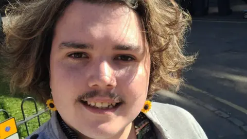 Call for free bus travel to help under-22s into work Dylan Lewis-Creser Dylan smiles in a selfie on a sunny day while wearing sunflower earrings