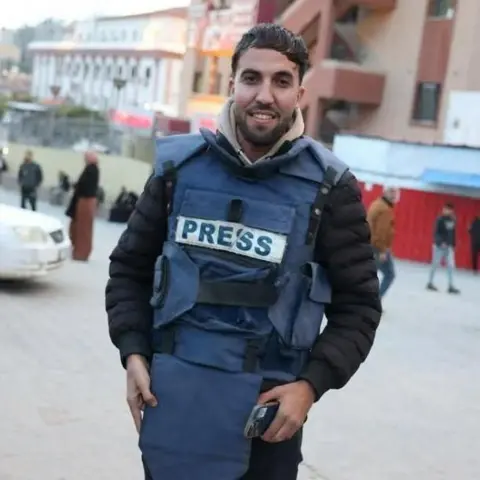 Israeli double strike on Gaza hospital Reuters A man smiles at the camera wearing a press vest and holding a mobile phone in his hand