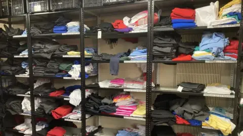 Free school uniform schemes demand is rising Telford Crisis Support Black metal shelves holding various labelled items of clothing in different colours