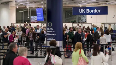 Record 111,000 UK asylum applications in past year, figures show Getty Images The UK border control area at Gatwick Airport. The white-walled hall is busy with people who are queuing in a long, winding line. Some are holding suitcases and passports. There is a large blue column in the middle of the room which says: "UK/EU passports" and a large sign hangs from the ceiling which reads "UK Border".