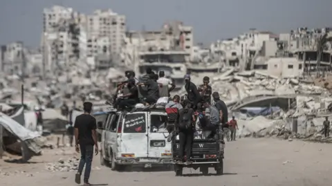 Gaza City evacuation inevitable, Israeli army warns Palestinians Getty Images Residents in Gaza City, with buildings destroyed by the Israeli attacks in the background, 24 August