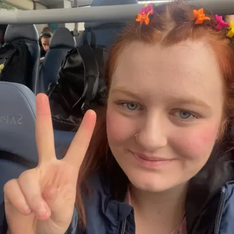Under-22s join call for free travel Maisy Moazzenkivi Maisy Moazzenkivi with short red hair with yellow orange and pink clips making a peace sign with her fingers while sitting on a bus