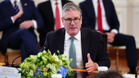 Starmer hails breakthrough on Ukraine EPA Keir Starmer sitting at glossed wooden table in White House meeting with other leaders. The camera is on him as he speaks. Starmer is gesturing with his left hand and is wearing a black blazer, a white shirt and a patterned blue tie. There are blue flowers in front of him on the table. Behind, sit three men against the wall - the heads are out of shot, but they are wearing suits, white shirts and a stripy navy and white tie, a red tie and a red tie respectively from left to right.