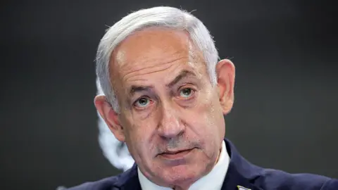 Gaza talks to focus on releasing all hostages in one go, Netanyahu hints ABIR SULTAN/POOL/AFP via Getty Images Headshot of Israeli Prime Minister Benjamin Netanyahu staring ahead wearing a dark suit.